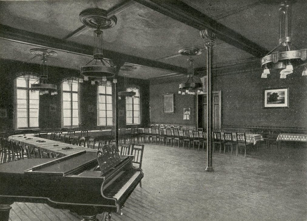 Historische Fotografie des Klubzimmers mit Flügel, langen Tischen und Deckenleuchtern